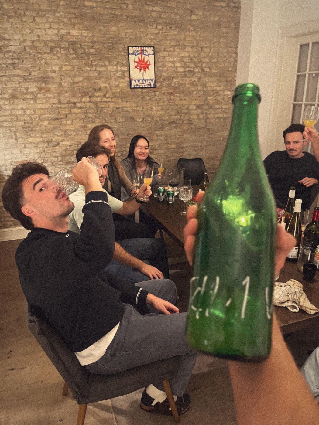 A table of friends raising glasses, one drinking from a crystal glass toward the camera