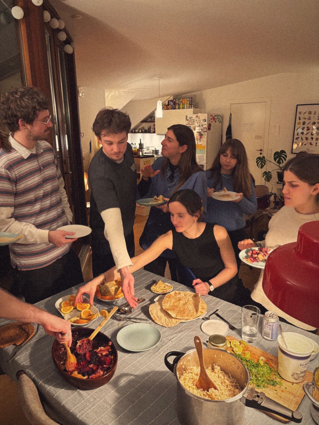 Guests crowding around a table of crumble, oranges, pancakes and rice