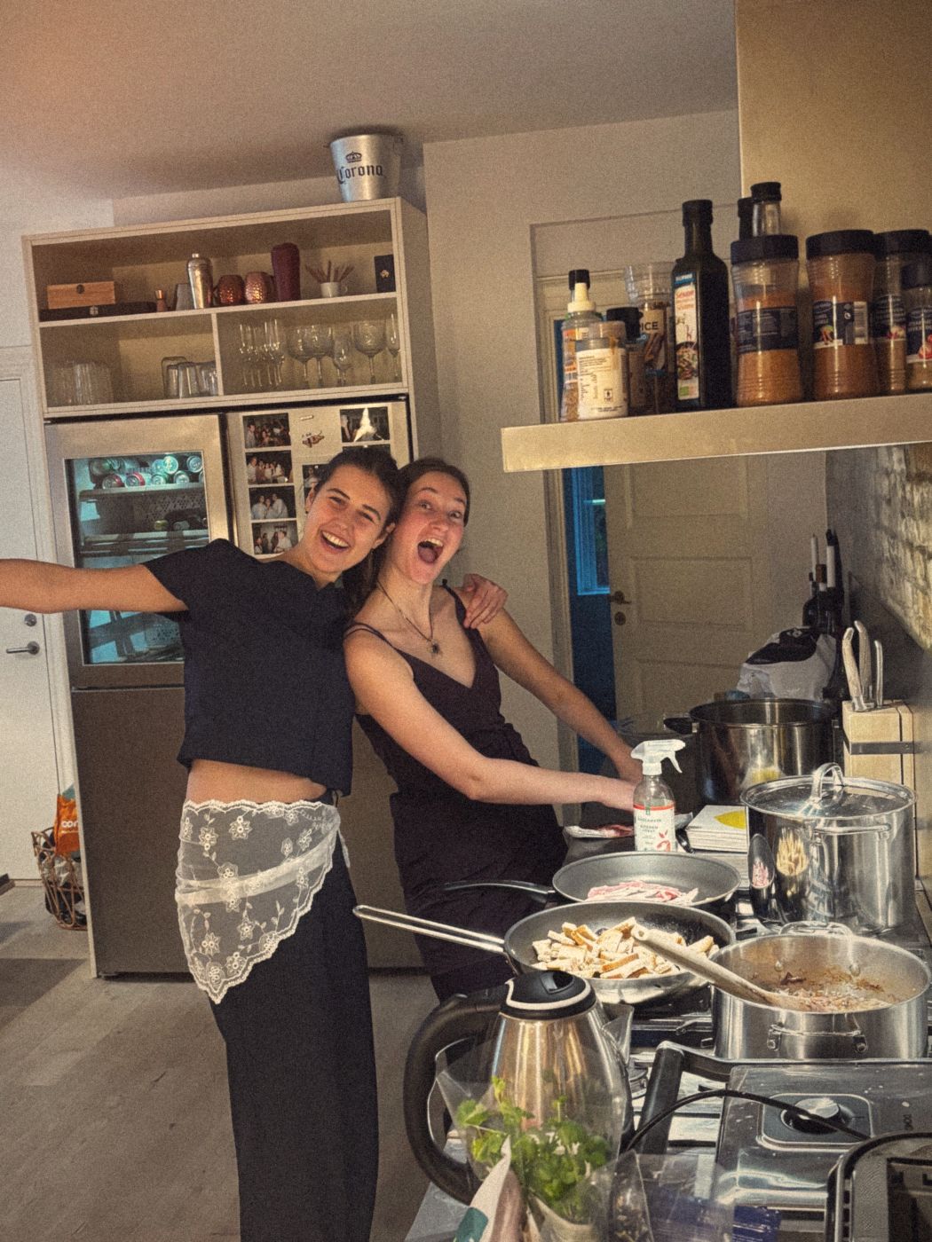 Two friends laughing in a kitchen while their pans are on the stove