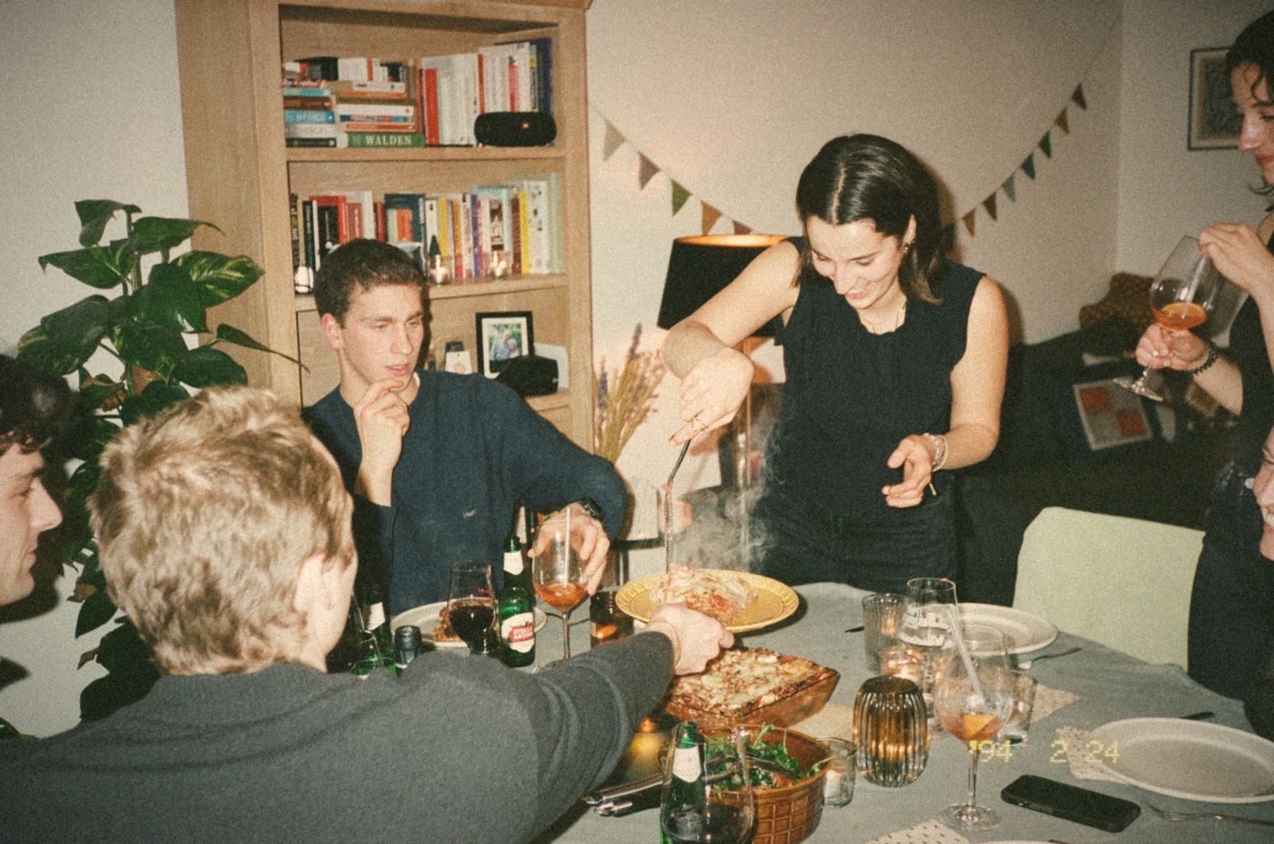 A host serving steaming lasagne to guests around a small table