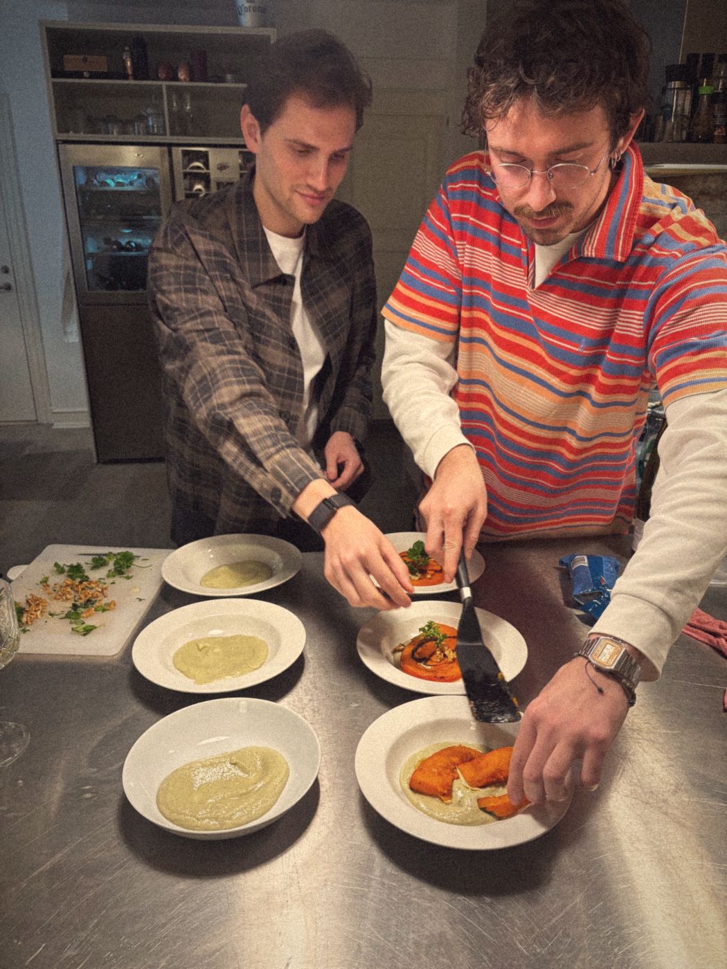 Two friends plating a starter of roasted pumpkin on purée with walnuts and parsley